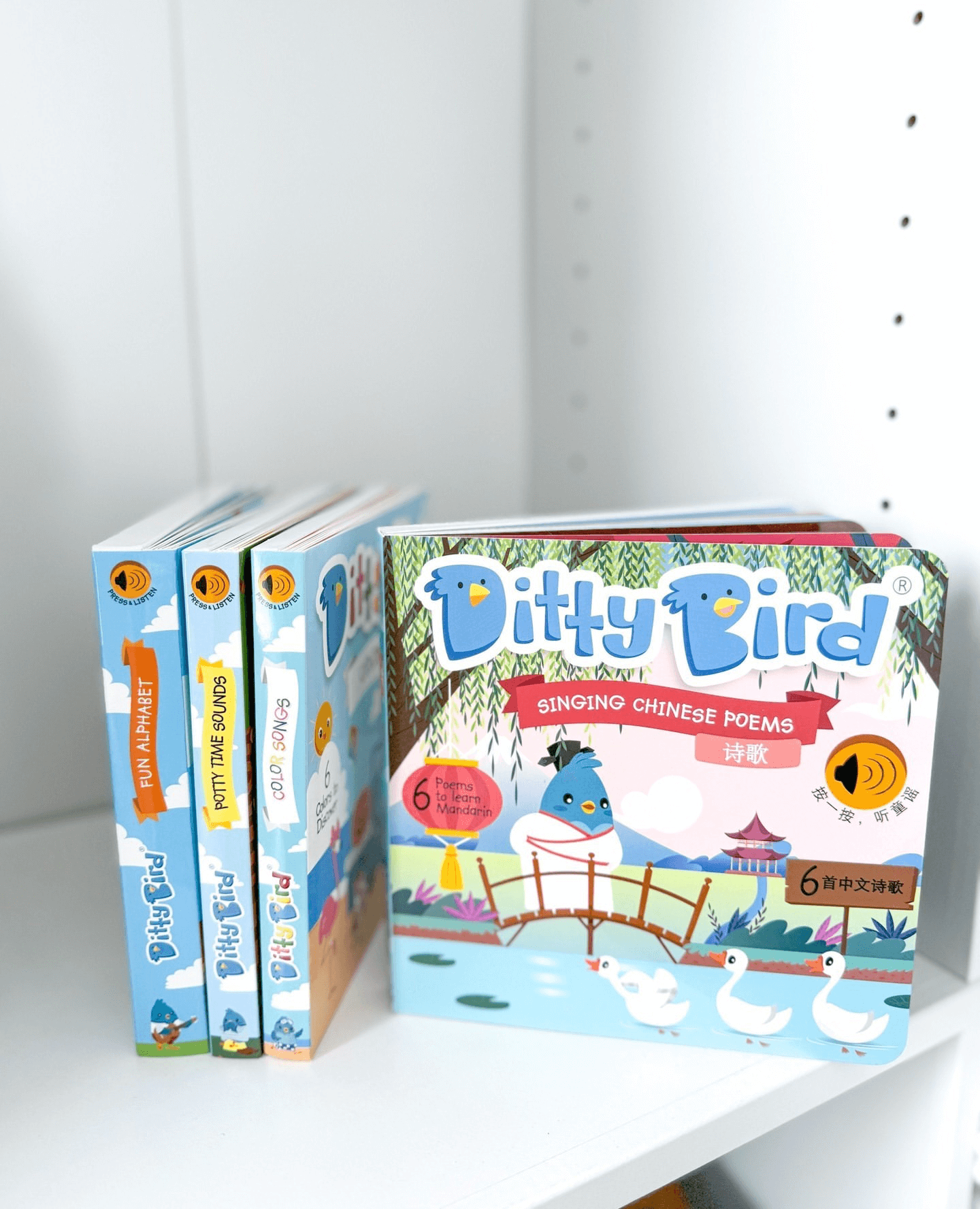 Three Ditty Bird children’s books stand upright on a white shelf beside a Ditty Bird Singing Chinese Poems (AG10 battery model) sound book, which has ducks, a bridge, and a blue bird on its cover.