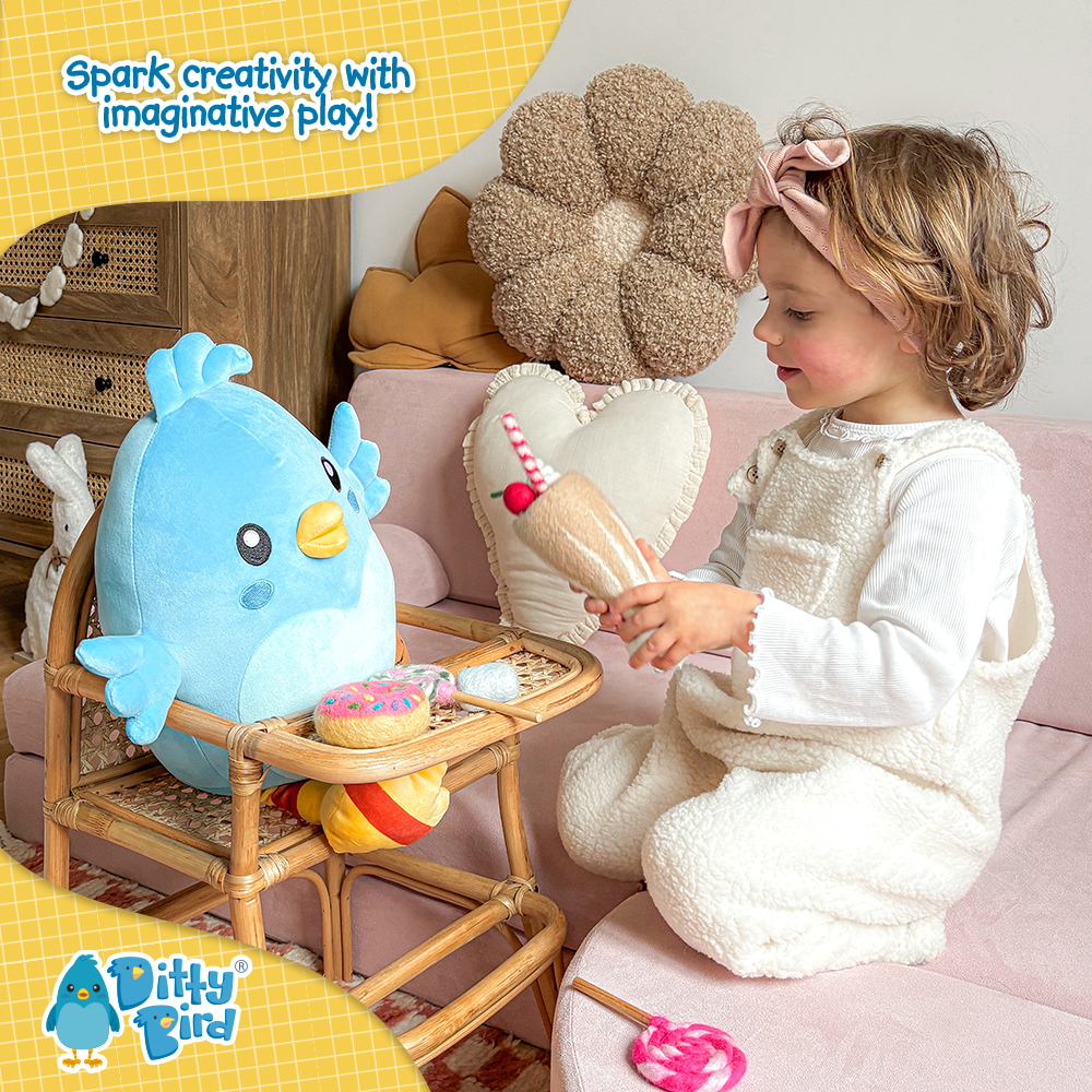 A young child in a white outfit serves pretend ice cream and donuts to the NEW! Ditty Bird Squishy Soft Plush by Ditty Bird on a small chair. The playful scene features the text: Spark creativity with imaginative play! above.