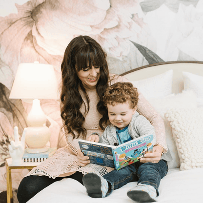 A woman with long brown hair and a young boy with curly hair smile together on a bed, enjoying Ditty Bird’s Classical Music—nurturing cognitive development through music in their cozy, charmingly decorated room.