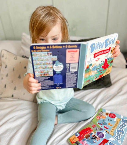 A young child sits on a bed, focused and captivated as they read Ditty Bird’s Dinosaur Sounds book. Another colorful book lies nearby while the fun dinosaur sounds from this interactive Ditty Bird book keep the child engaged.