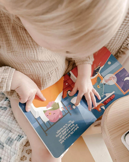 A young child in a beige textured outfit sits and uses their finger to follow along while reading Ditty Bird Potty Time Sounds | AG10, a potty training book with cartoon animals and bright backgrounds that make potty time fun and engaging.